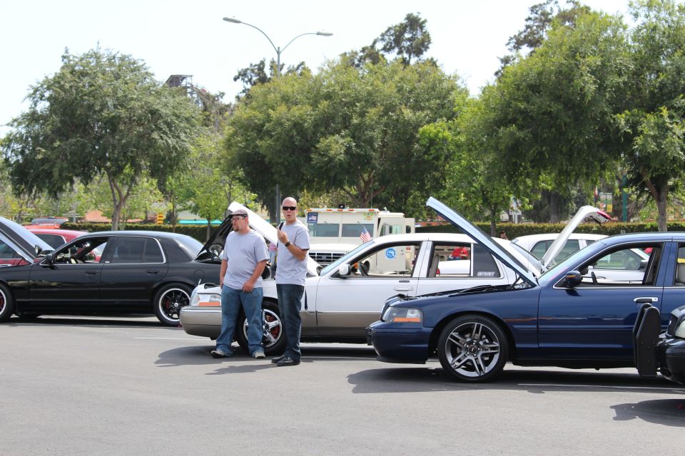 Two men standing among lowered sedans with open hoods at a car meet