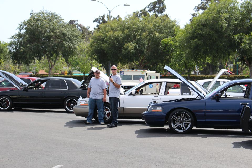 Two men beside lowered sedans with open hoods and chrome wheels