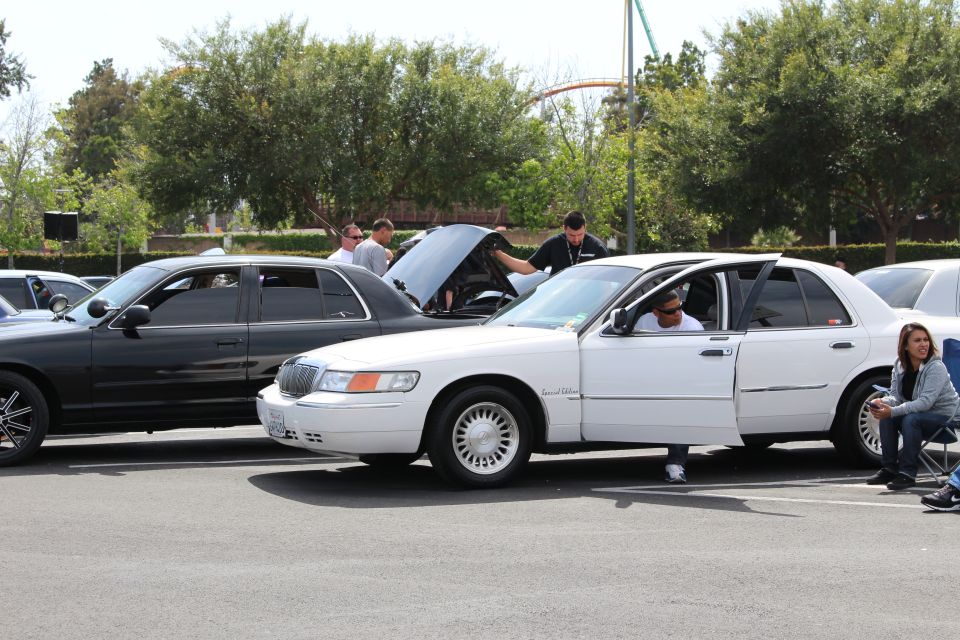 White Mercury Grand Marquis with people, black sedan and open hood behind
