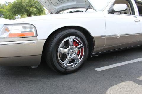 Front wheel of a white two-tone sedan with chrome five-spoke wheel and red brake caliper
