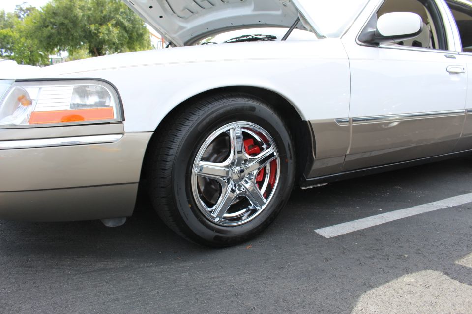 Front wheel of a white two-tone sedan with chrome five-spoke wheel and red brake caliper