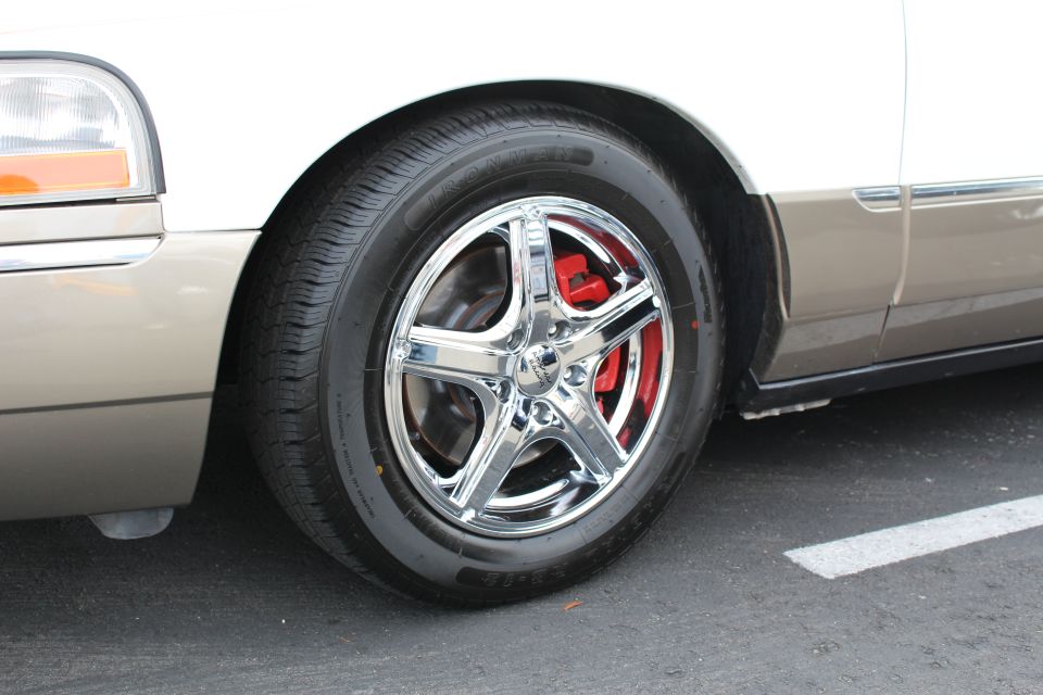 Chrome five-spoke wheel and red caliper on a tan and white sedan in a parking lot