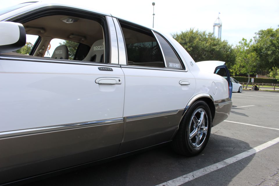 Rear three-quarter of a lowered white and tan four-door sedan with chrome wheels