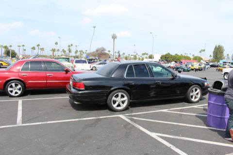 Rear three-quarter of a black lowered four-door sedan in a packed car-show lot