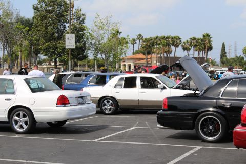 White, two-tone and black full-size sedans displayed with open hoods at a show