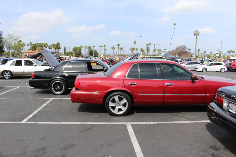 Red Ford sedan parked beside a black sedan with open trunk at an outdoor car show