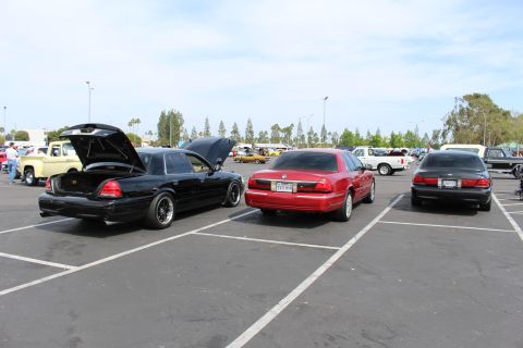 Three sedans parked in a row at an outdoor car show, one with trunk open