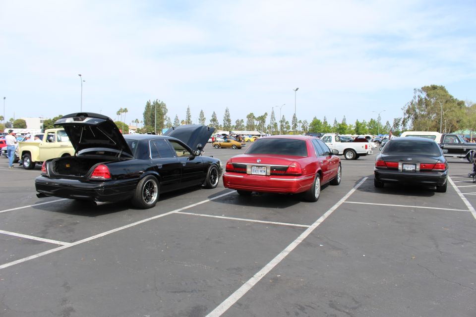 Three sedans parked in a row at an outdoor car show, one with trunk open