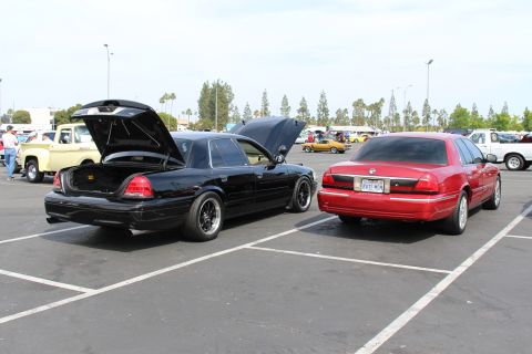 Black sedan with open trunk parked next to a red sedan in a sunny lot