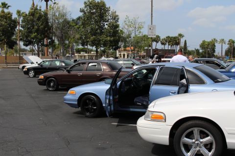 Light blue sedan with door open parked in a row with brown and white sedans