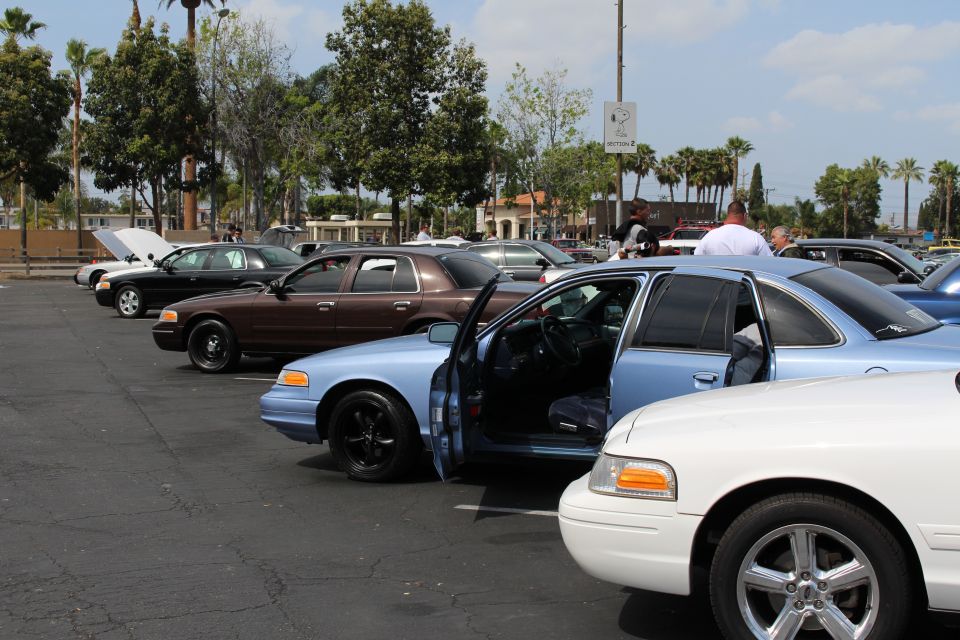 Light blue sedan with door open parked in a row with brown and white sedans