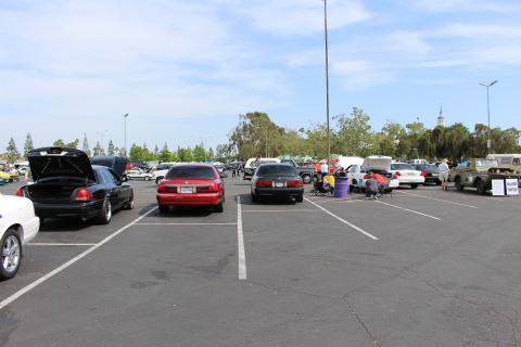 Wide view of a car show parking lot with many sedans and people