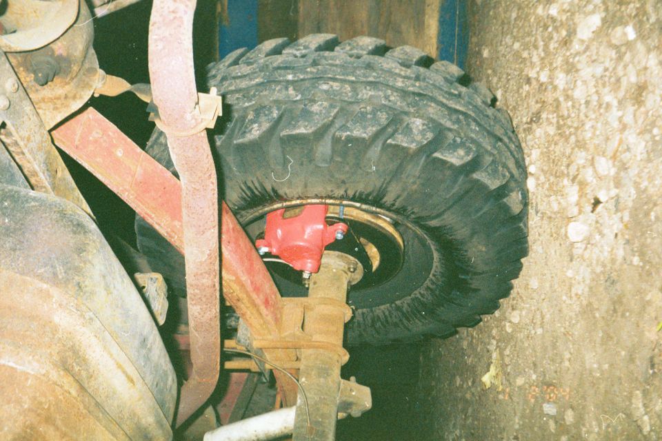 Red disc brake caliper on a solid axle behind a mud-terrain tire during a brake conversion