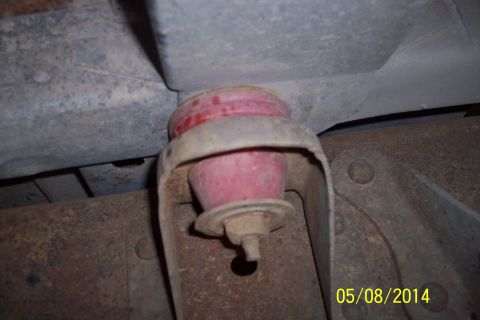 1978 Ford Bronco - A close-up view of a red suspension bushing, showing its mounting hardware and surrounding rusty frame components.