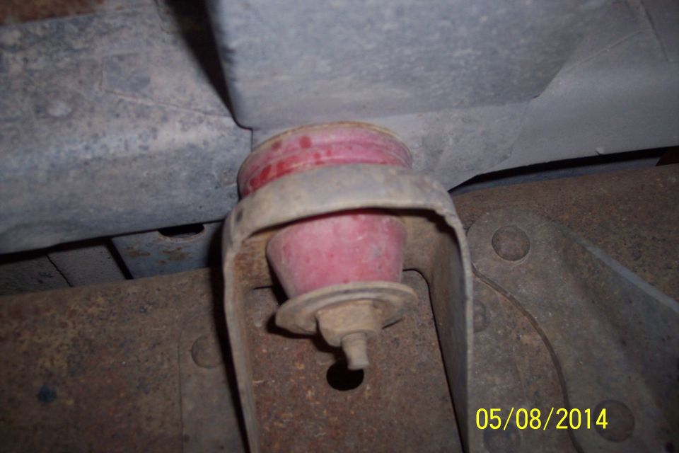 Close-up of a red suspension bushing on a rusty metal bracket, likely from the undercarriage of a vehicle