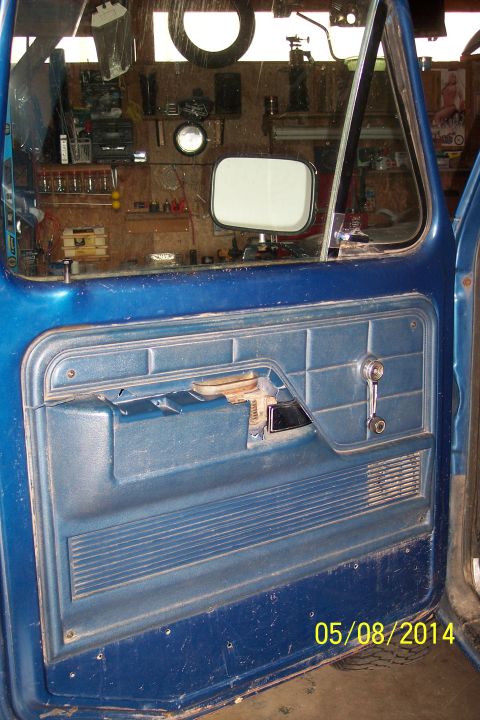 1978 Ford Bronco - Interior view of a blue truck door panel, with a workshop visible through the window.