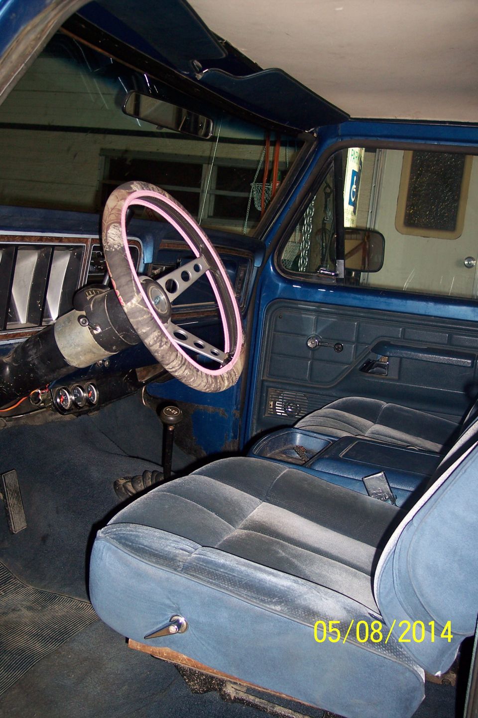 Blue velour interior of a 1978 Ford Bronco with a patterned steering wheel and dashboard