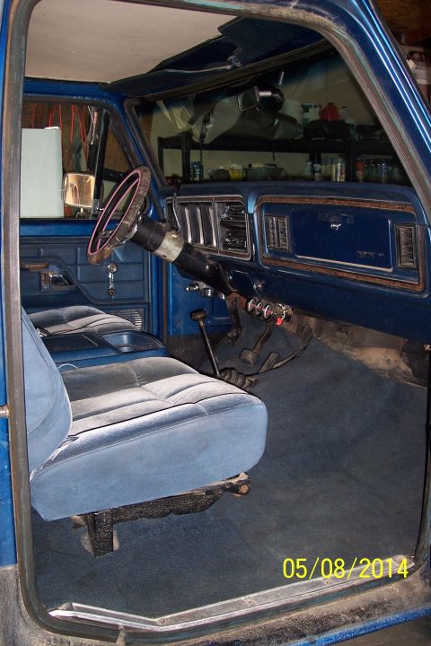 1978 Ford Bronco - The interior of a blue 1978 Ford Bronco is shown, plush seats and a wood-grain dashboard.