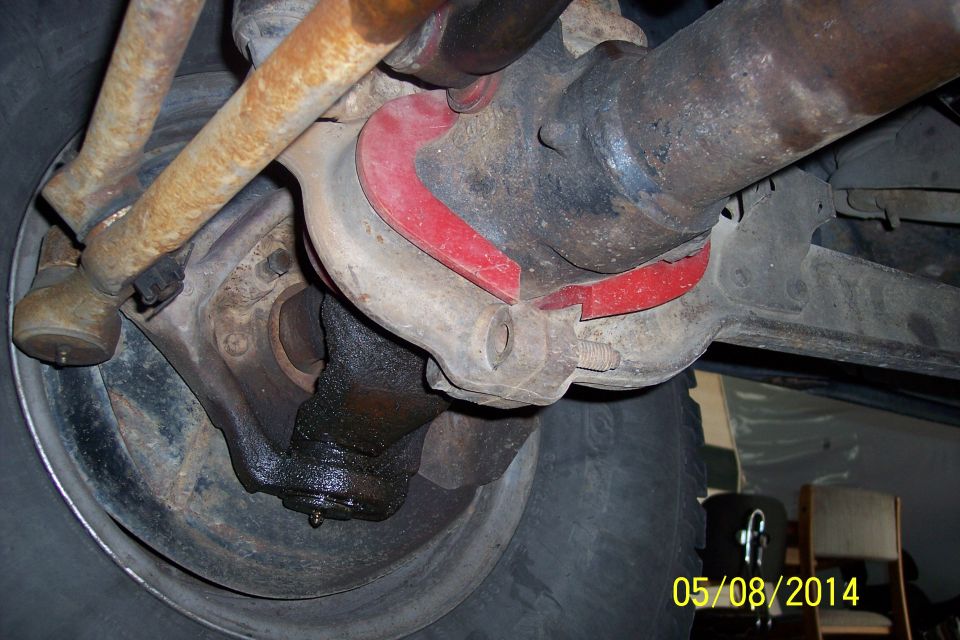 Close-up of vehicle's front suspension components, including tie rod ends and red polyurethane bushings