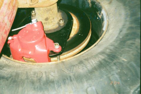 1979 Ford Bronco - Close-up of a vehicle's brake system, showing a red caliper and rotor assembly.