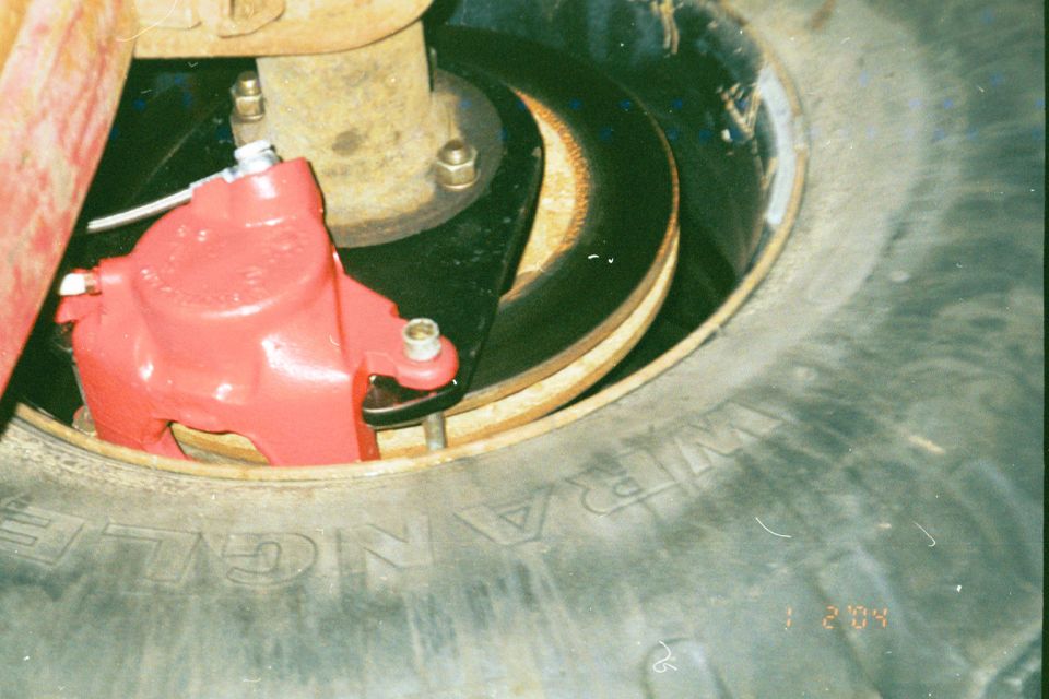 Red disc brake caliper and rusty rotor inside a Goodyear Wrangler tire