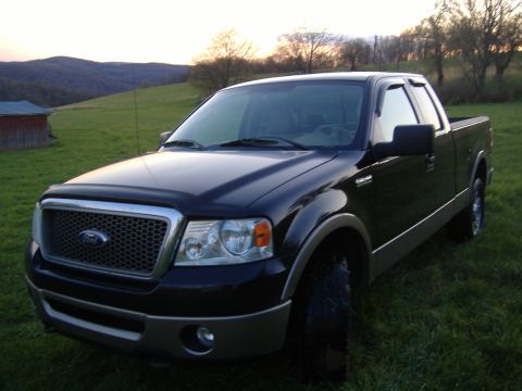 2007 Ford F-150 - A black Ford F-150 pickup truck is parked in a grassy field with hills in the background during sunset.