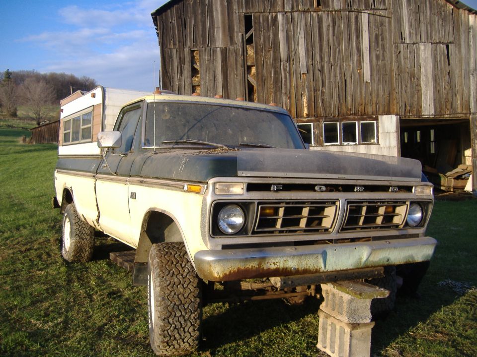1975 Ford F-150 pickup truck with a camper shell parked in front of a barn