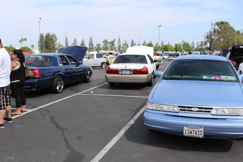 Light blue Ford sedan front beside a dark blue sedan and people in a lot