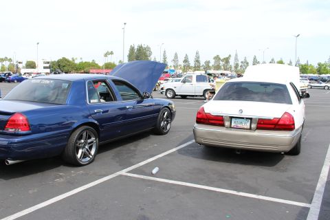 Dark blue sedan with open hood beside a two-tone white and gold Mercury
