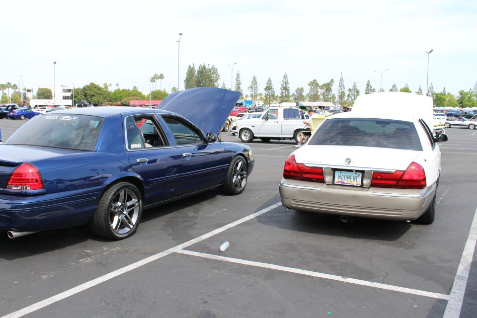 Dark blue sedan with open hood beside a two-tone white and gold Mercury