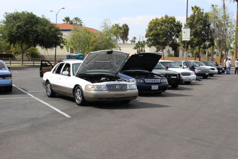 White and gold Mercury sedan with open hood leading a row of cars