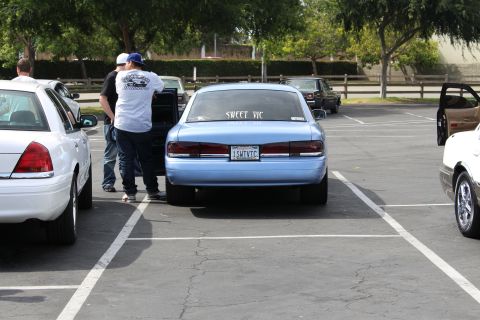 Rear of a light blue sedan with SWEET VIC window lettering and people nearby