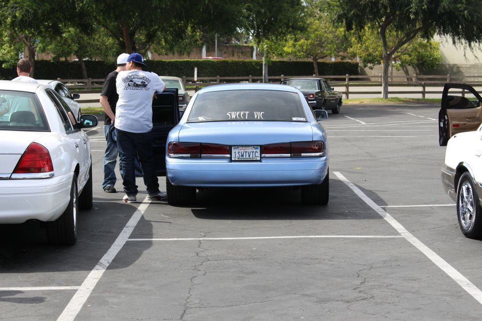 Rear of a light blue sedan with SWEET VIC window lettering and people nearby
