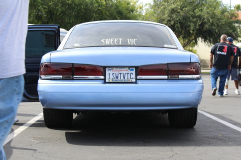 Rear of a light blue SWEET VIC sedan with people walking by in a lot