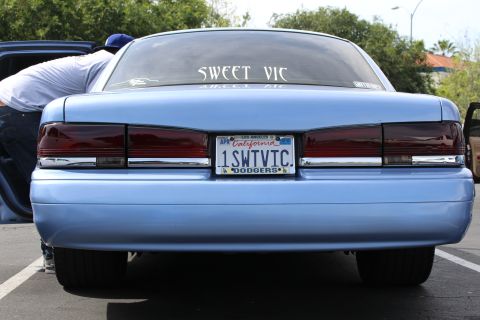 Rear of light blue sedan with California plate reading 1SWTVIC and SWEET VIC rear window decal