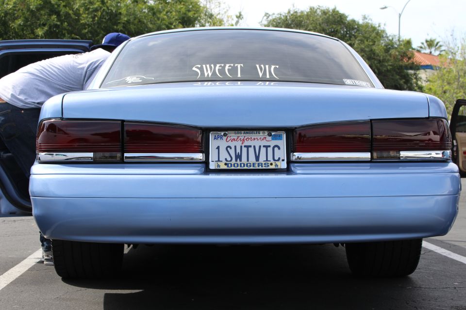 Rear of light blue sedan with California plate reading 1SWTVIC and SWEET VIC rear window decal