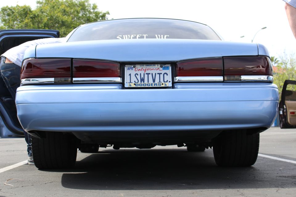 Low rear three-quarter view of light blue sedan with SWEET VIC window decal and 1SWTVIC plate
