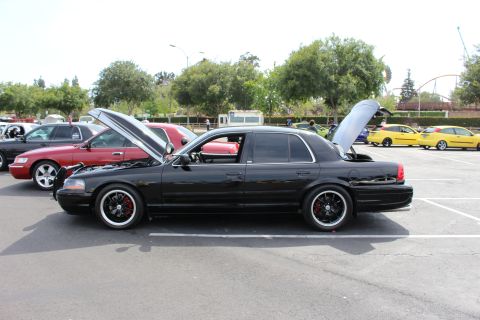 Side profile of lowered black full-size sedan with black multi-spoke wheels at a car meet