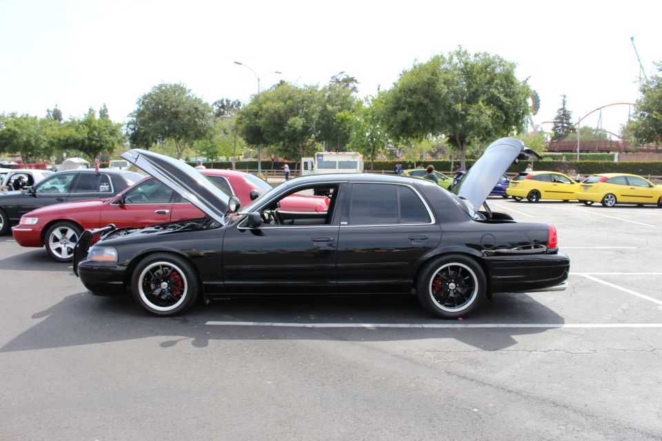 Side profile of lowered black full-size sedan with black multi-spoke wheels at a car meet