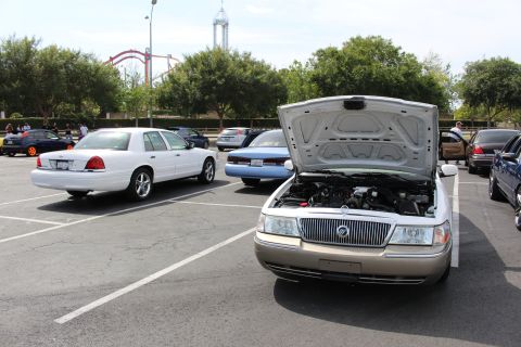 Silver sedan with hood open showing Mercury emblem grille, parked among cars near amusement park