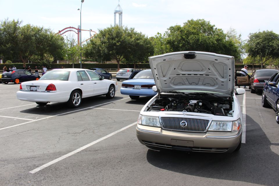 Silver sedan with hood open showing Mercury emblem grille, parked among cars near amusement park