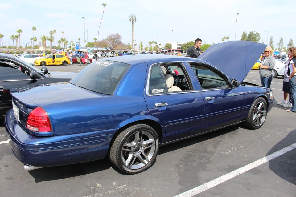 Rear three-quarter of blue full-size sedan with hood up on large polished wheels at car show