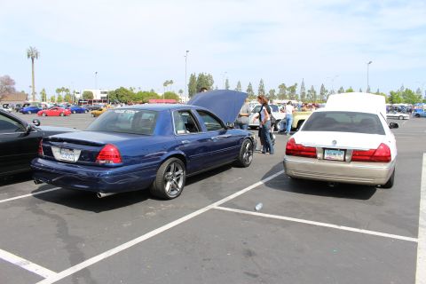 Blue sedan with hood up beside a gold sedan with white trunk in parking-lot car meet