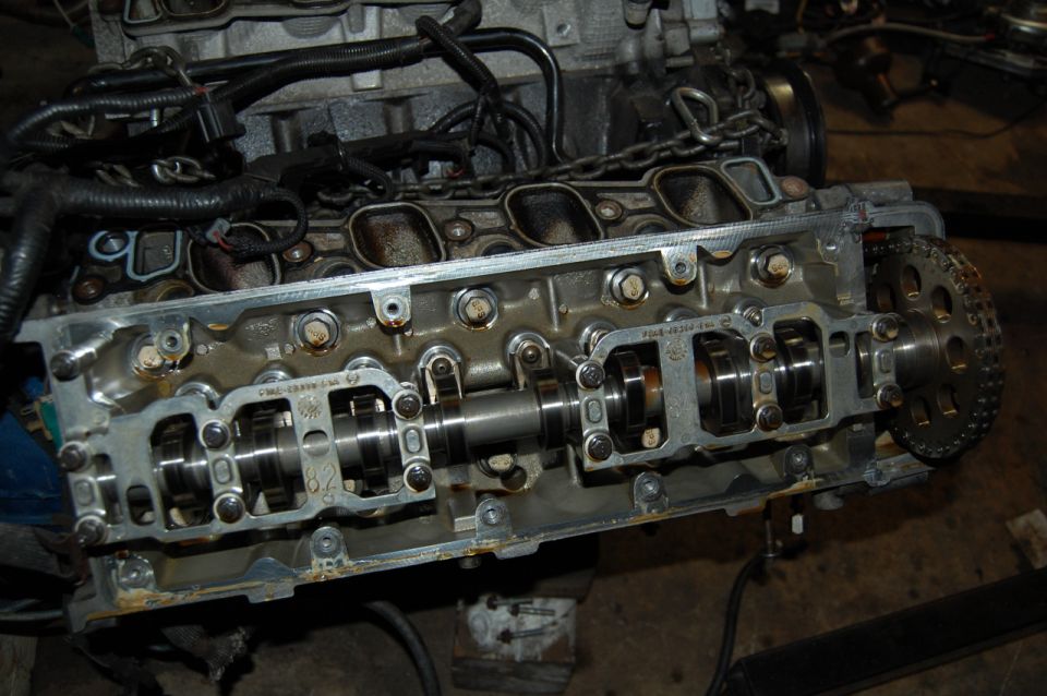 Disassembled V8 cylinder head with camshaft, rocker arms, and timing chain on bench