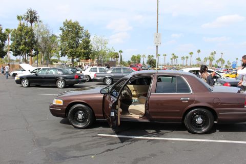 Brown full-size sedan with open door and tan interior on black steel wheels at car meet
