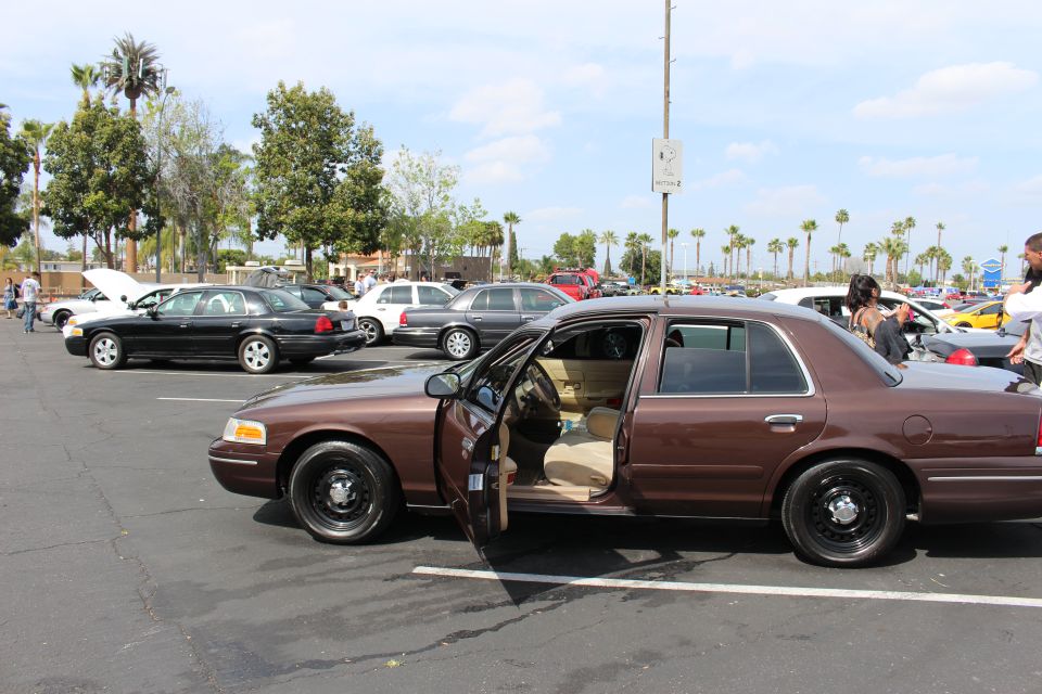 Brown full-size sedan with open door and tan interior on black steel wheels at car meet