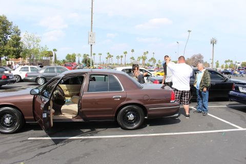 Brown sedan with open doors and tan interior, people standing beside it in parking lot