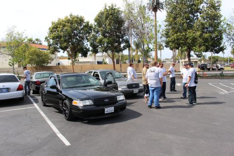 Black Ford sedan parked at angle with group of people standing beside it in parking lot