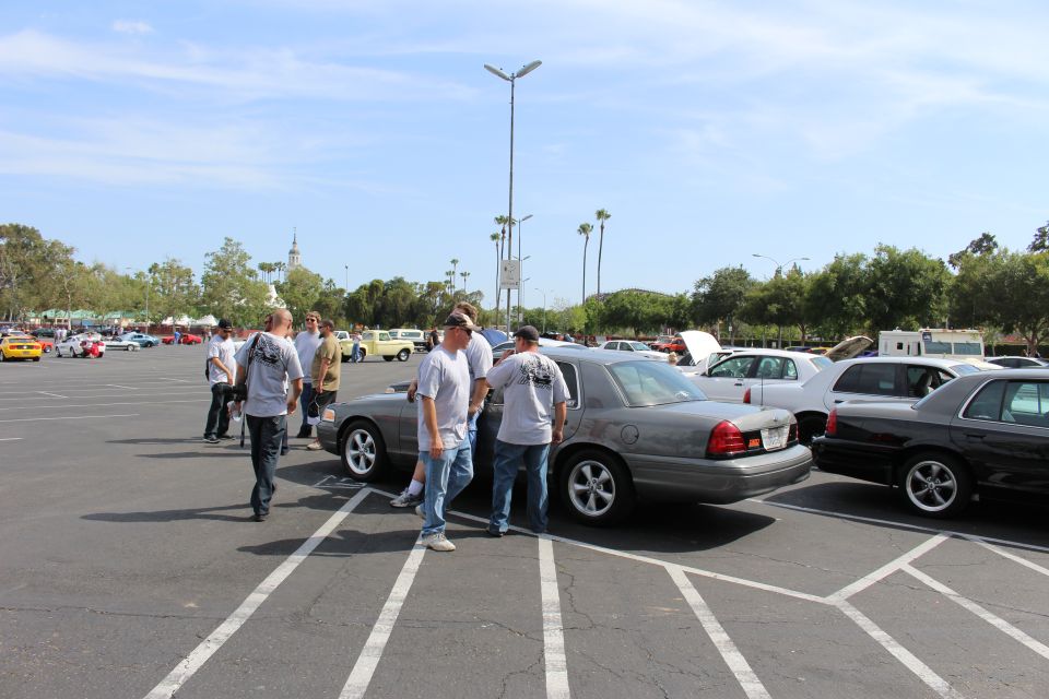 People walking among silver sedans in a large parking lot car meet with palm trees