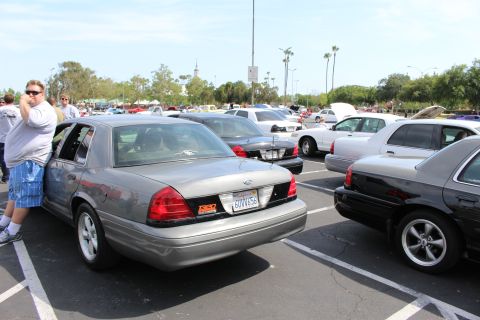 Rear three-quarter of silver sedan with Ford emblem in crowded parking-lot car meet